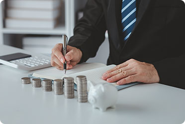 A man in a suit writing on paper with coins and a calculator, illustrating asset protection planning.