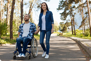 A woman walking beside a man in a wheelchair on a road.