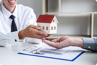 A man passing a house model to another man showing Real Estate concept