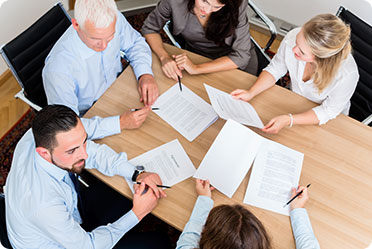 Board Of Directors meeting with business people around a table, engaged in discussion with papers.